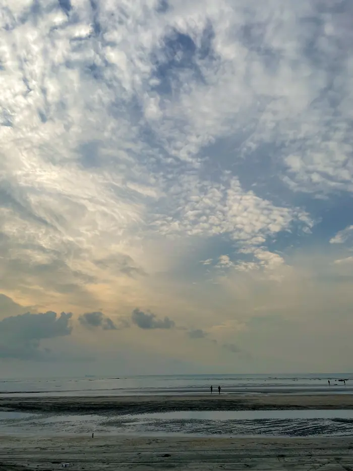 A broad shoreline under a tall bank of cloud, figures small in the distance