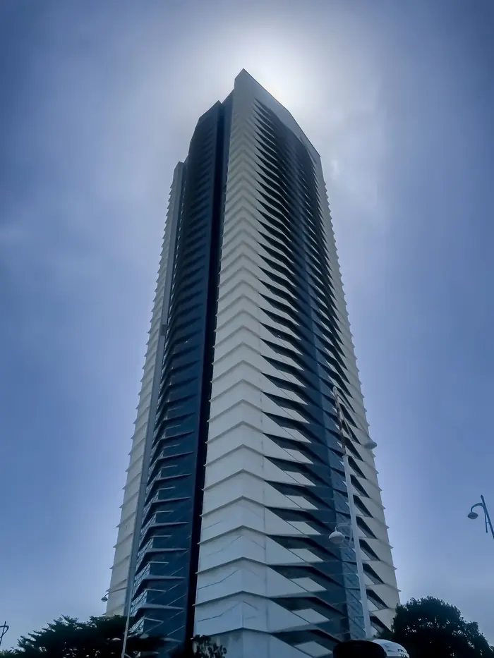 A residential tower shot from its base, balconies receding toward a flared sun